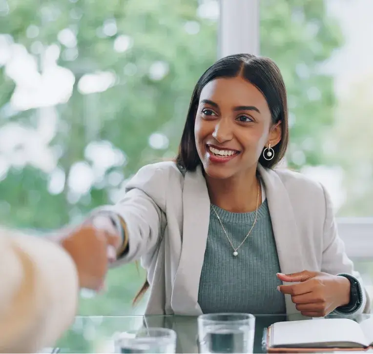 Smiling woman shaking hands across a desk at a job interview