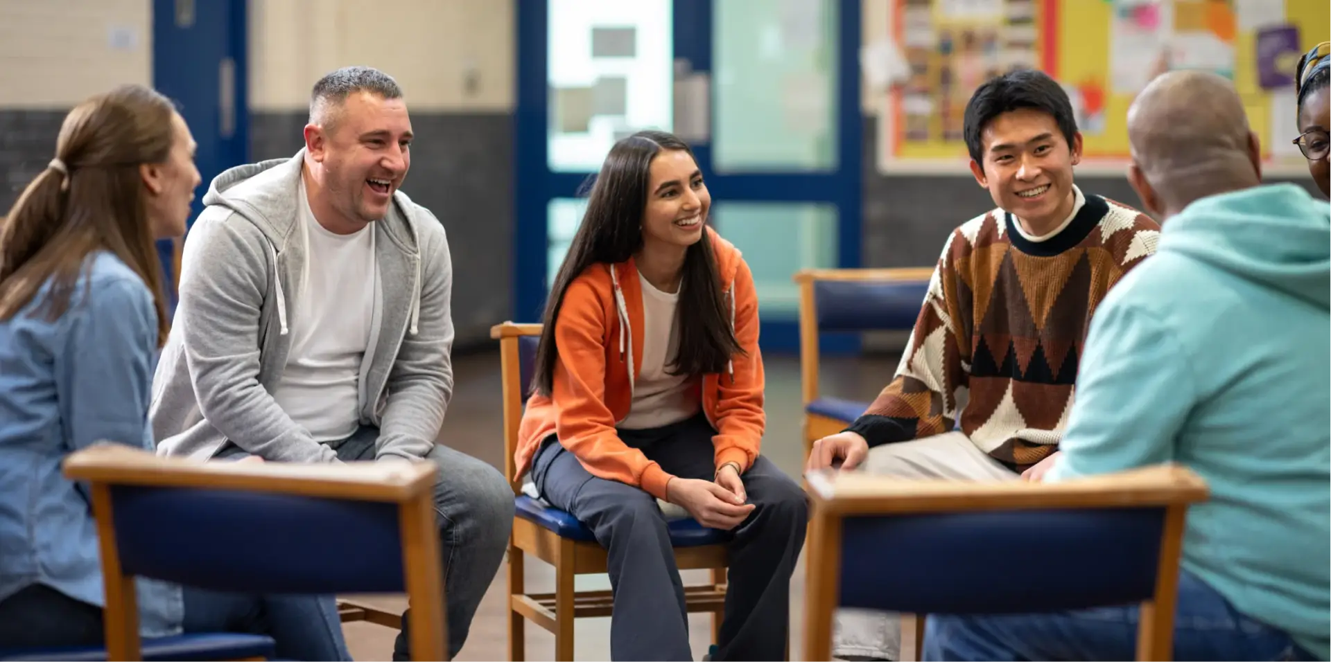 Local residents laughing and chatting in a circle of chairs at a community hall session