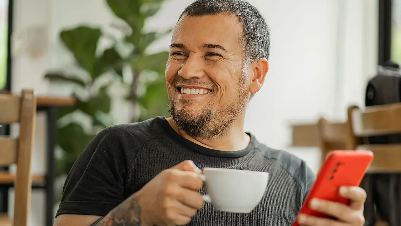 Smiling man holding a coffee and his phone while taking a break in a cafe