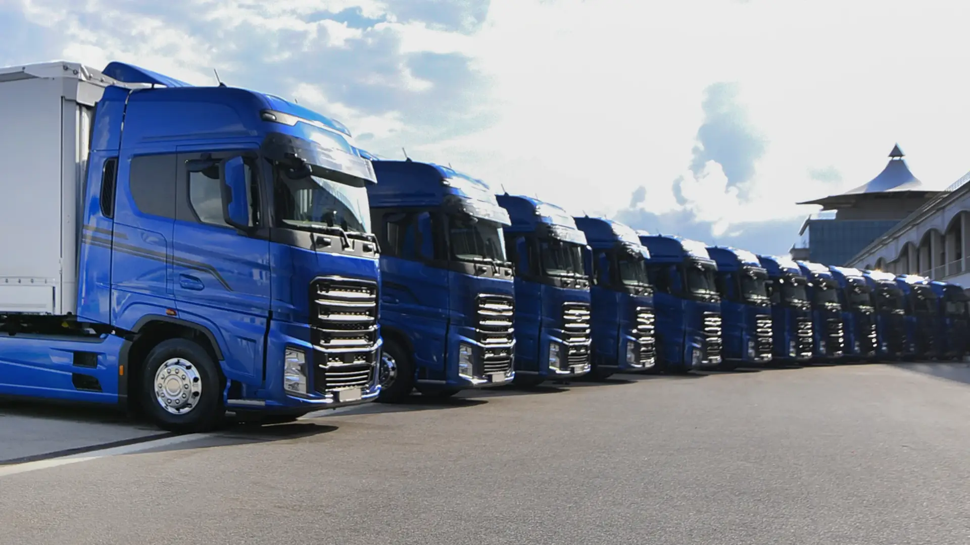 Row of blue electric trucks parked in a line awaiting charging
