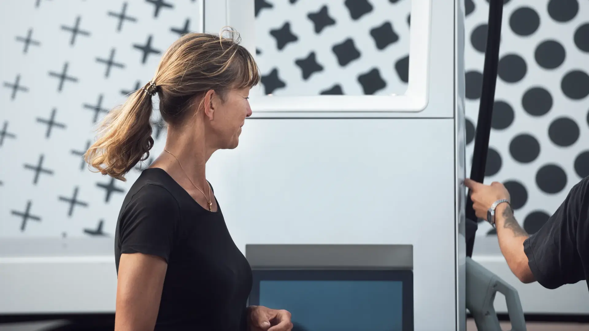 Woman using the touchscreen on a charging unit at a multi-energy hub while a driver takes the charging cable
