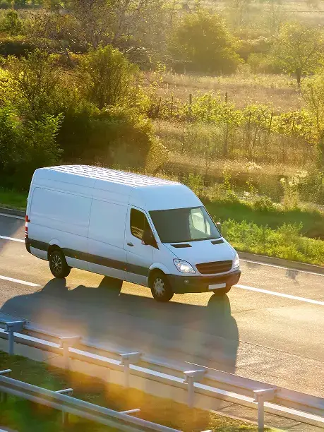 White delivery van driving along a road lined with hedgerows in early morning light